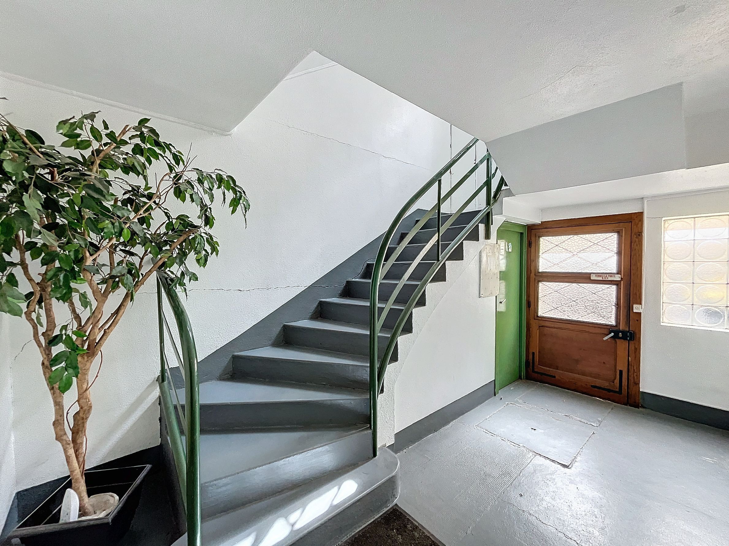 Eine Treppe mit Metallgeländer führt zu einer Zwischenebene, einem Blumentopf und einer Holztür mit Fenster.