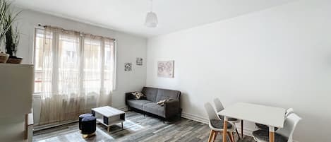 A modern living room with a grey sofa, a small table, and a dining area with chairs.