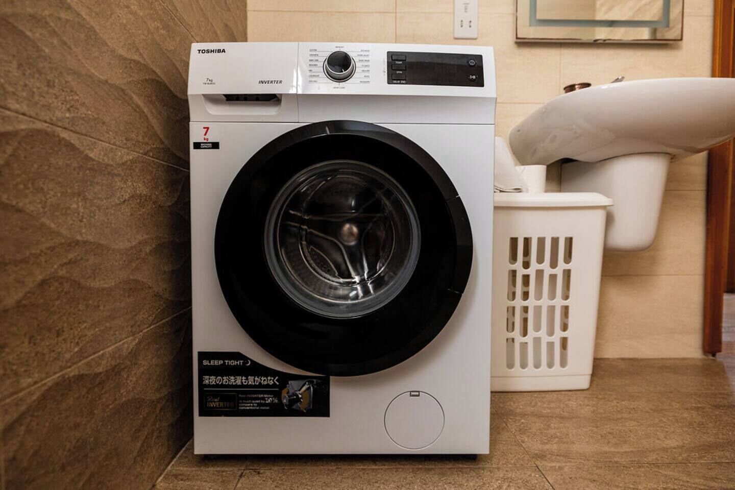 Eine Toshiba Waschmaschine mit Bedienfeld, einem Hinweis mit der Aufschrift 'Schlaf gut' und einem weißen Wäschekorb in der Nähe.