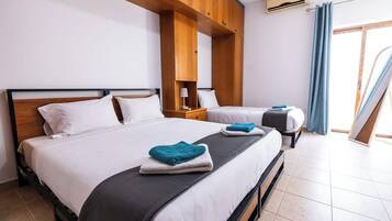 Ein Hotelzimmer mit einem großen Bett, einem kleineren Bett, einem Holz-Kopfteil, einem Nachttisch, einer Lampe und einem Fenster mit Vorhängen.