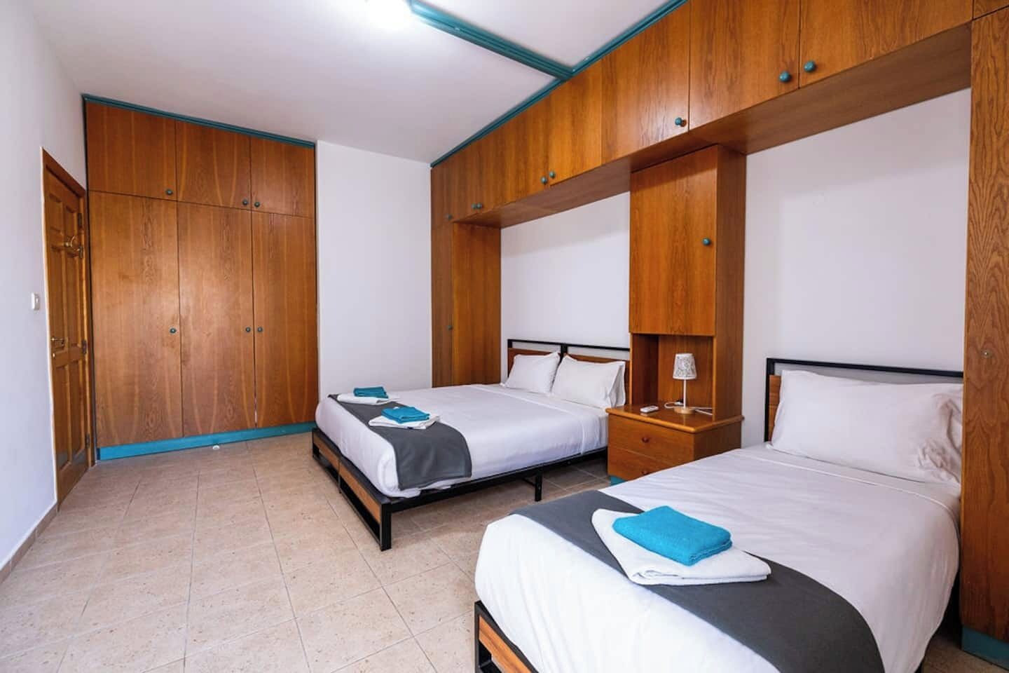 A hotel room with two beds, wooden wardrobes, and a tiled floor.