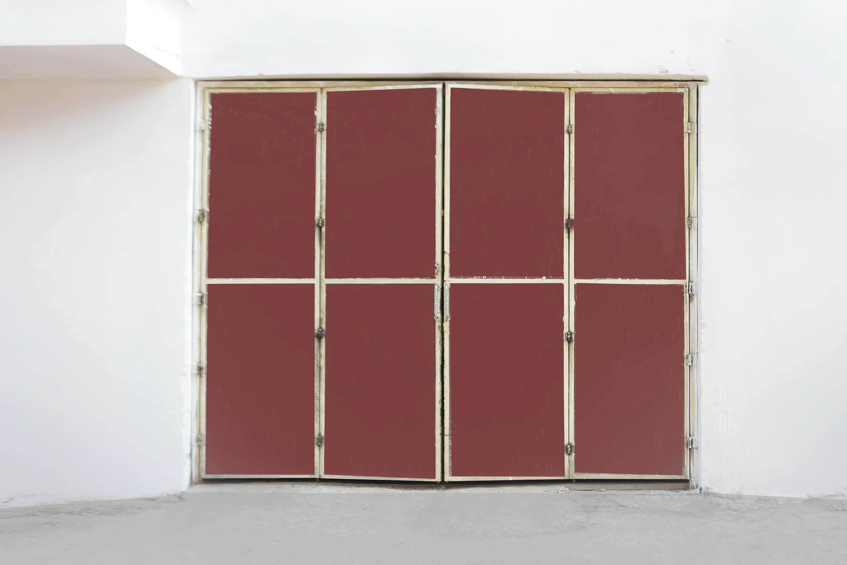 A closed, red-framed door with a white wall and concrete floor.
