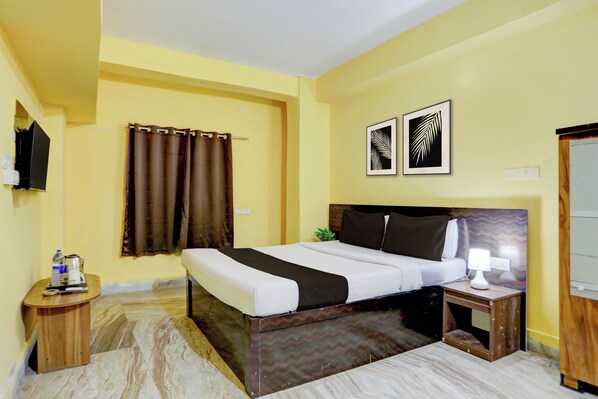 A hotel room with a bed, a bedside table, a lamp, a TV, and two framed pictures on the wall.