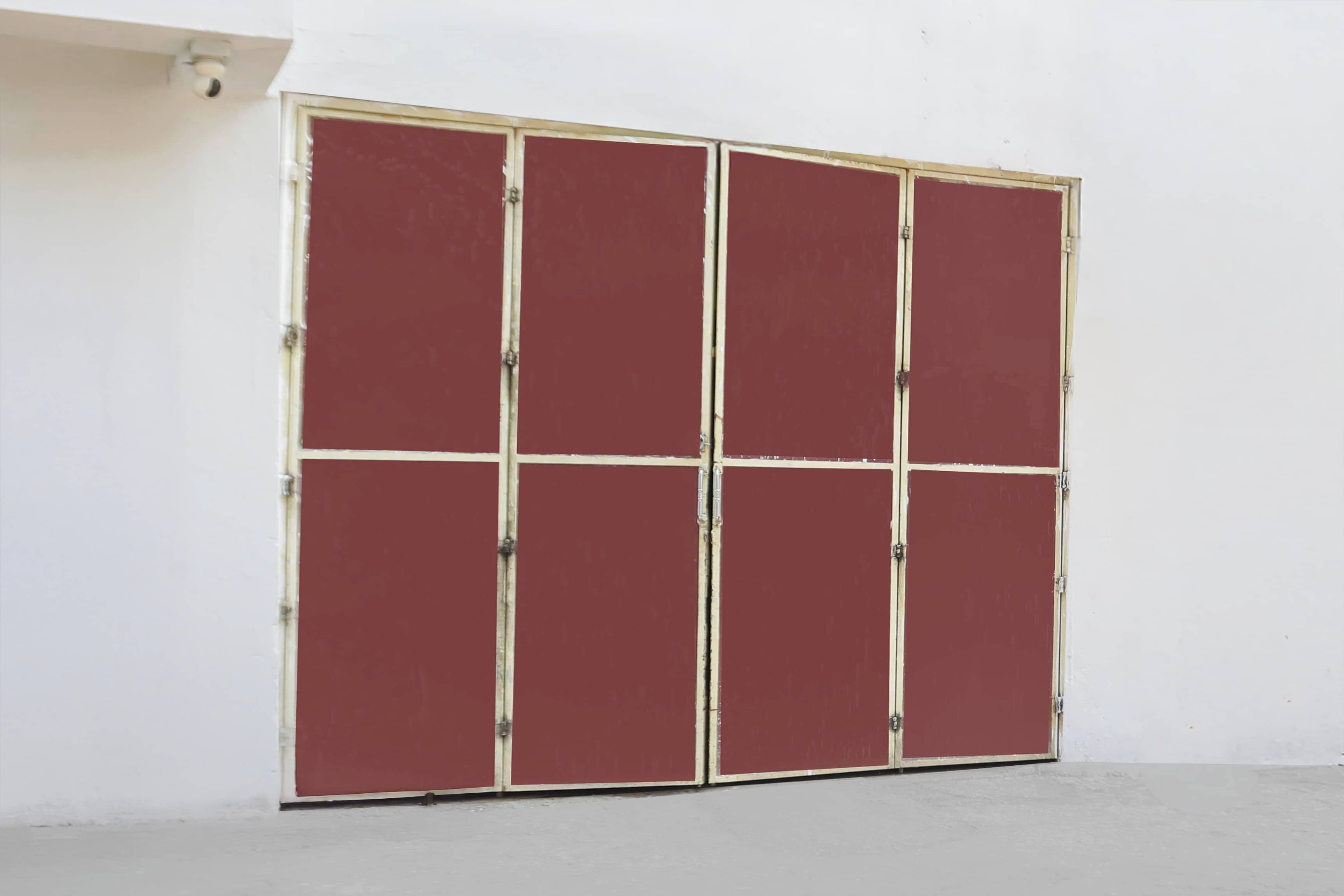 A closed, red-framed door with a white wall and a concrete floor.