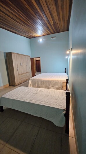 A room with a wooden ceiling, a bed with a white mattress, a wardrobe, and a door leading to another room. - Property in Ibiúna with a stunning lake. (Ibiúna)
