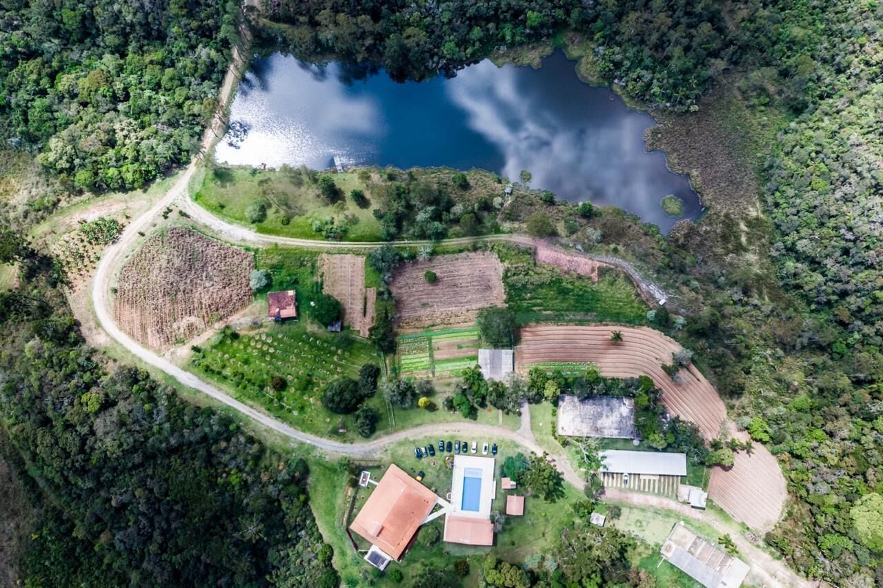 An aerial view of a property with a swimming pool, tennis courts, and a surrounding forested area.