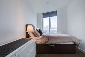 A bedroom with a bed, bedside table, lamp, and a window with a city view. - Luxury City Apartment in Central London (London)