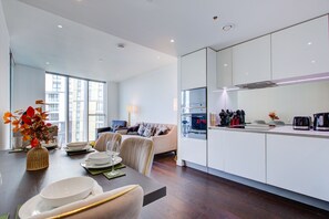 A modern kitchen with white cabinets, a dining area with a table set for two, and a sofa in the background. - Luxury City Apartment in Central London (London)