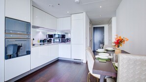 Een moderne keuken met witte kasten, een eethoek met een tafel gedekt voor twee personen, en zicht op de woonkamer.