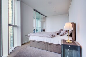 A modern bedroom with a bed, bedside lamp, and a view of the city through large windows. - Luxury City Apartment in Central London (London)