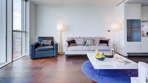 Een moderne woonkamer met een bank, fauteuil en salontafel, met een stadszicht door grote ramen.