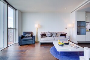A modern living room with a sofa, armchair, and coffee table, featuring a city view through large windows. - Luxury City Apartment in Central London (London)