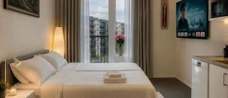 A hotel room with a bed, bedside table, lamp, and a small table with books and flowers.