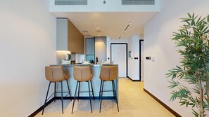 A modern kitchen with a bar area, three bar stools, and a potted plant. - Sleek 1 Bed with Burj Khalifa View l Business Bay (Business Bay)