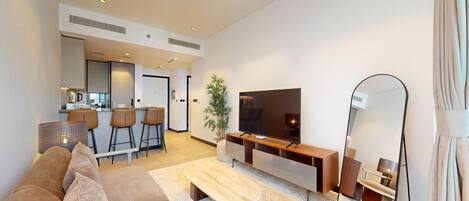 A modern living room with a sofa, a flat-screen TV, a coffee table, and a dining area with chairs.