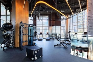 A gym with exercise equipment, large windows, and a high ceiling. - Sleek 1 Bed with Burj Khalifa View l Business Bay (Business Bay)