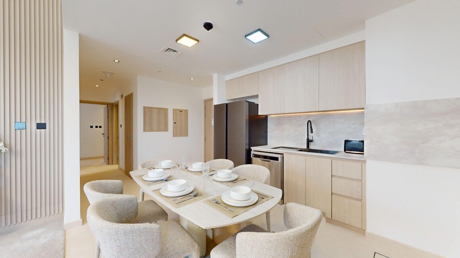 A modern kitchen with a dining area, featuring a long table set for four, light-colored cabinetry, and built-in appliances.