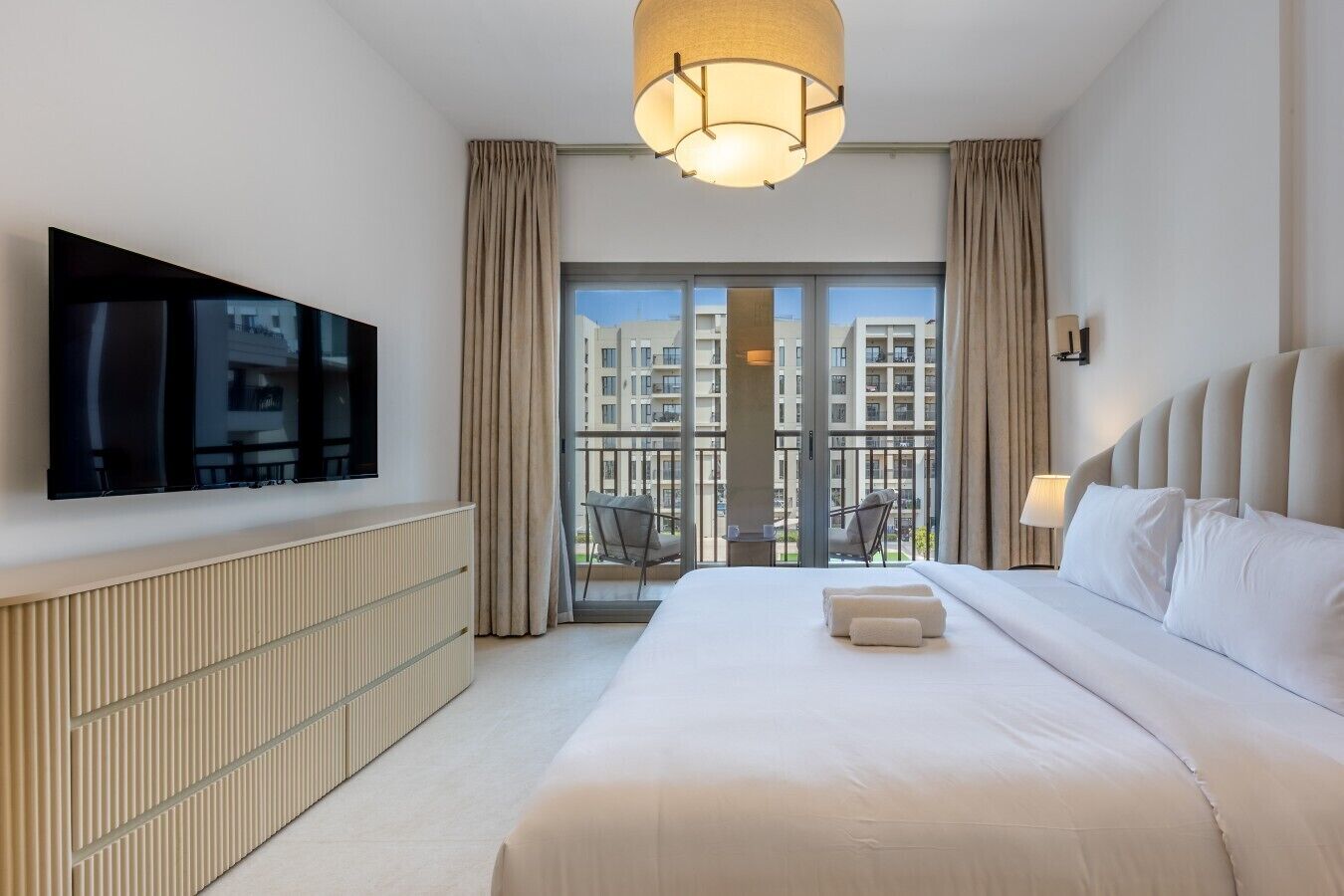 Une chambre d’hôtel dotée d’un grand lit, d’un téléviseur à écran plat fixé au mur, d’un balcon offrant une vue sur la ville et d’un luminaire moderne.