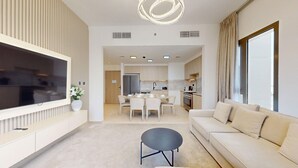 A modern living room with a flat-screen TV, a sofa, a coffee table, and a dining area with chairs. - Aesthetic 2 Bed in Townsquare l Pool and Gym (Town Square)