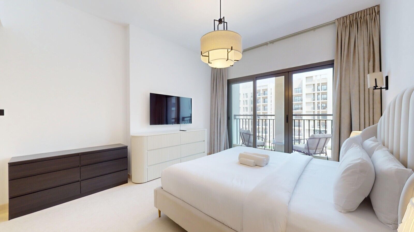 A modern hotel room with a large bed, a flat-screen TV, a bedside table, and a view of the city through the balcony.
