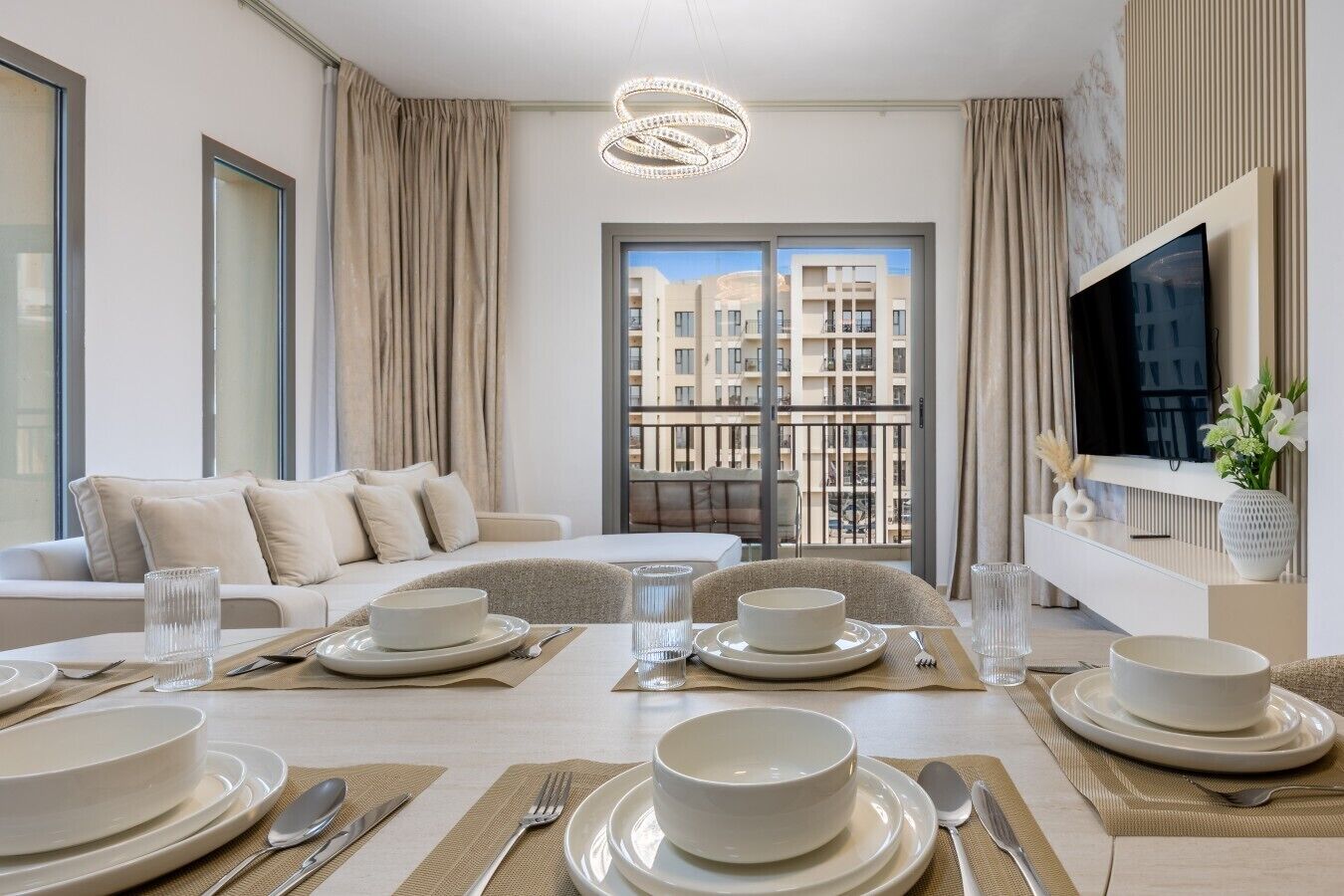A modern living room with a dining area, a sofa set, a television, and a balcony with a city view.