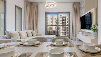 A modern living room with a dining area, a sofa set, a television, and a balcony with a city view.