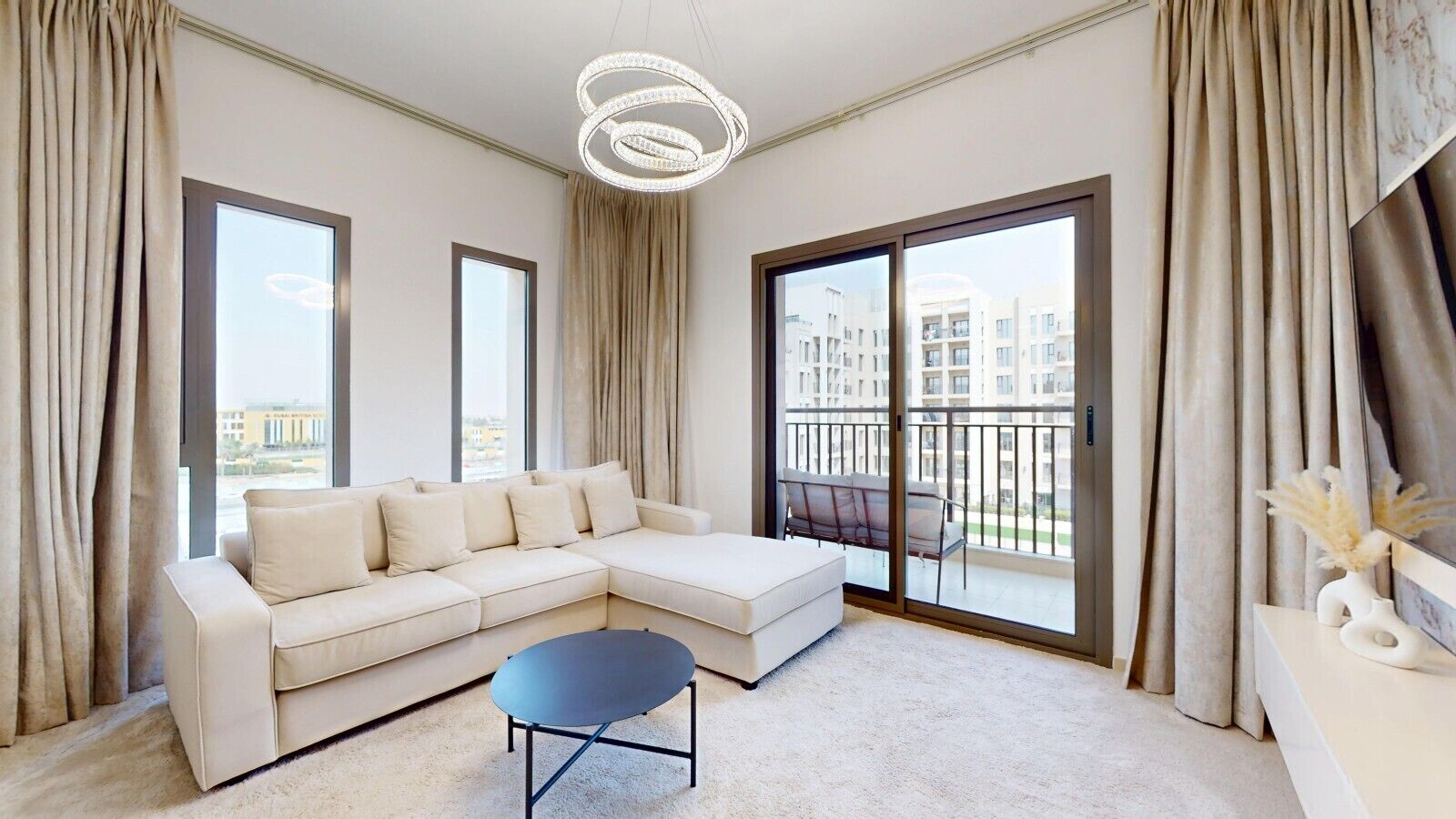 Sala de estar moderna com sofá modular, mesa de centro redonda e varanda com vista para edifícios.