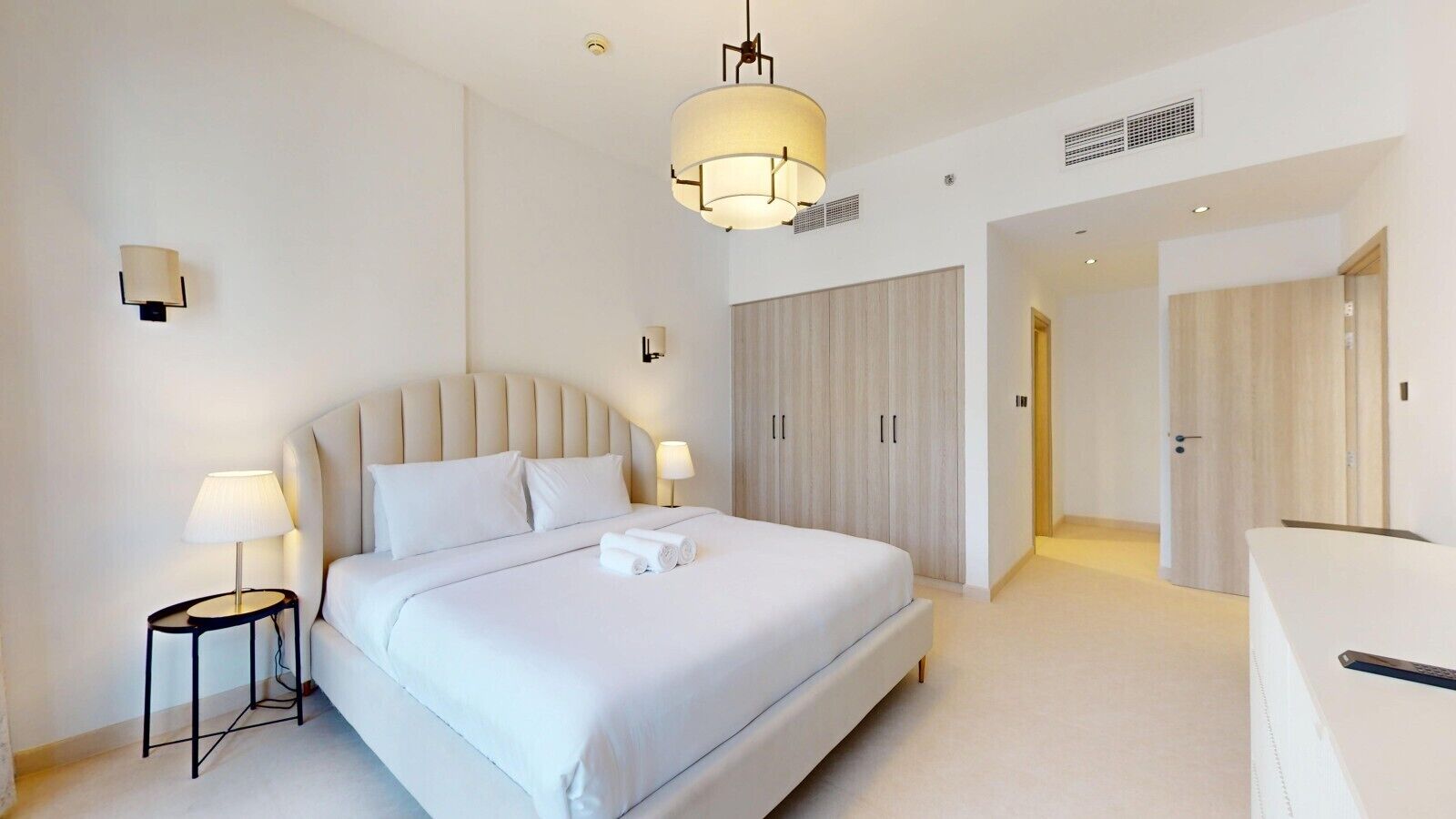Een moderne hotelkamer met een groot bed, nachtlampjes, een kledingkast en een zichtbare badkamer door een open deur.