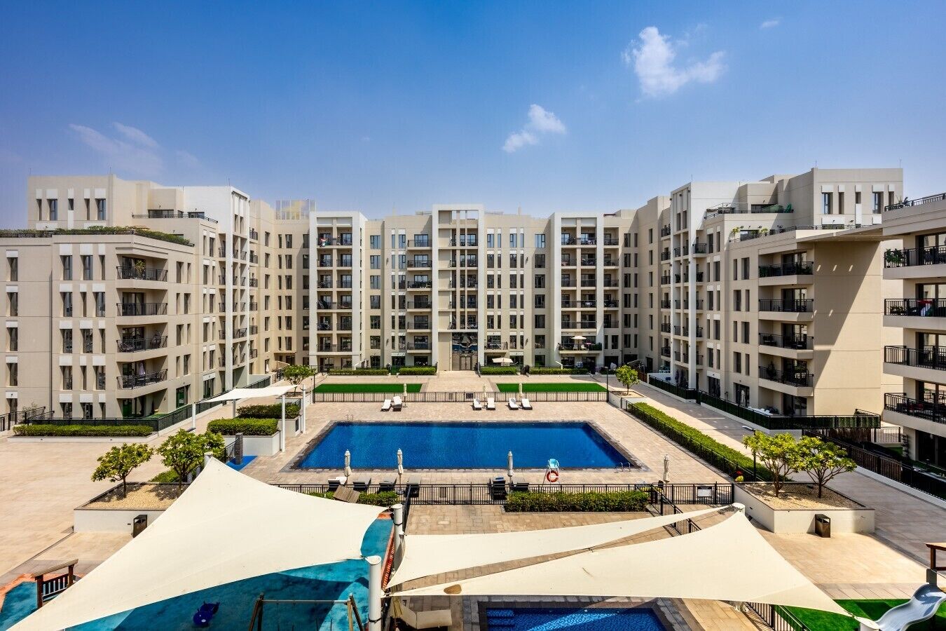 A modern apartment complex with a central swimming pool, multiple balconies, and a well-maintained outdoor area.
