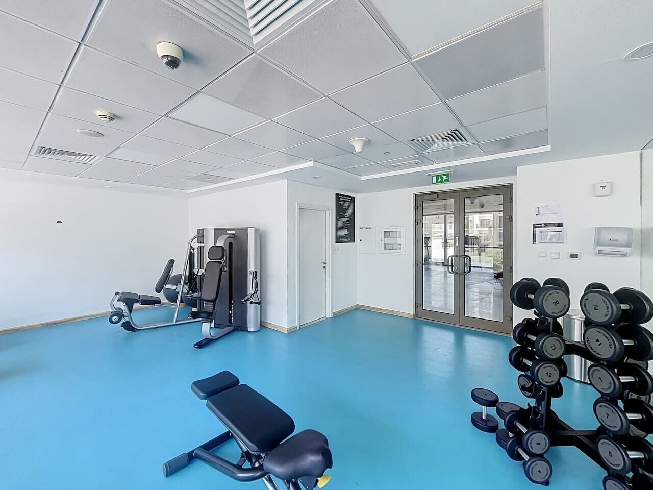 A gym with exercise equipment, a blue floor, and a glass door leading outside.