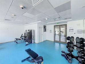 Ein Fitnessstudio mit Trainingsgeräten, einem blauen Boden und einer Glastür, die nach draußen führt.