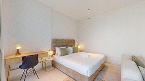 Ein Hotelzimmer mit Bett, Nachttisch, Lampe, Stuhl und Schreibtisch mit Lampe.
