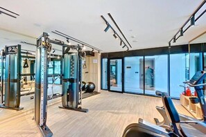A modern gym with cardio equipment, weight machines, and a large window providing a view of the outdoors. - Chic Studio with Canal View l Business Bay (Business Bay)