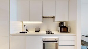 A modern kitchen with white cabinetry, a stainless steel sink, a toaster, a microwave, and a built-in oven. - Chic Studio with Canal View l Business Bay (Business Bay)