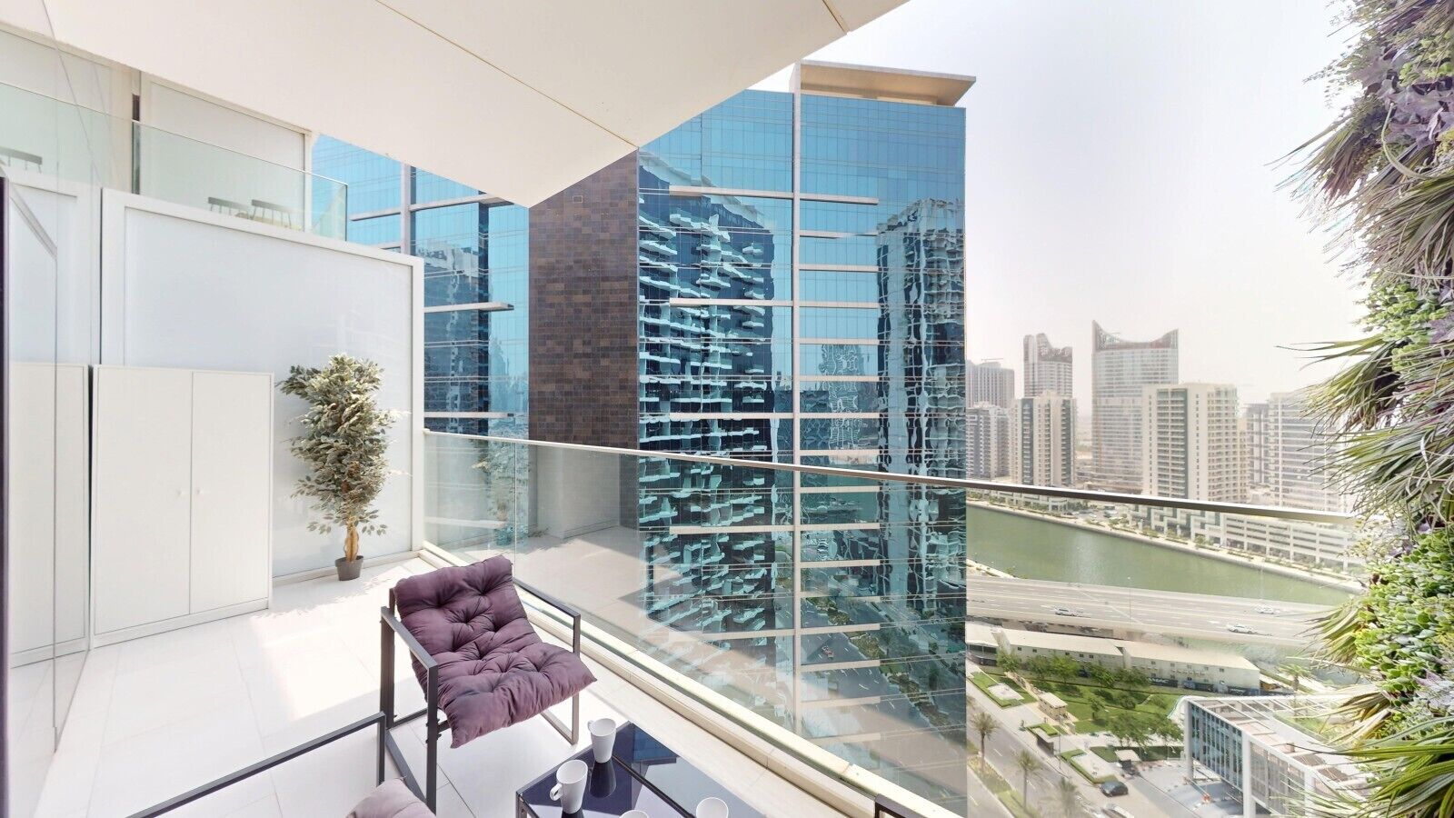 A modern balcony with a glass railing, a purple chair, and a view of a cityscape and river.