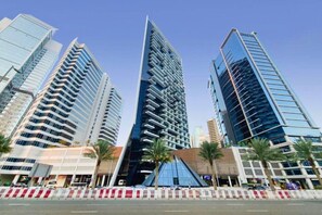 A modern urban skyline with high-rise buildings, palm trees, and a clear sky. - Chic Studio with Canal View l Business Bay (Business Bay)