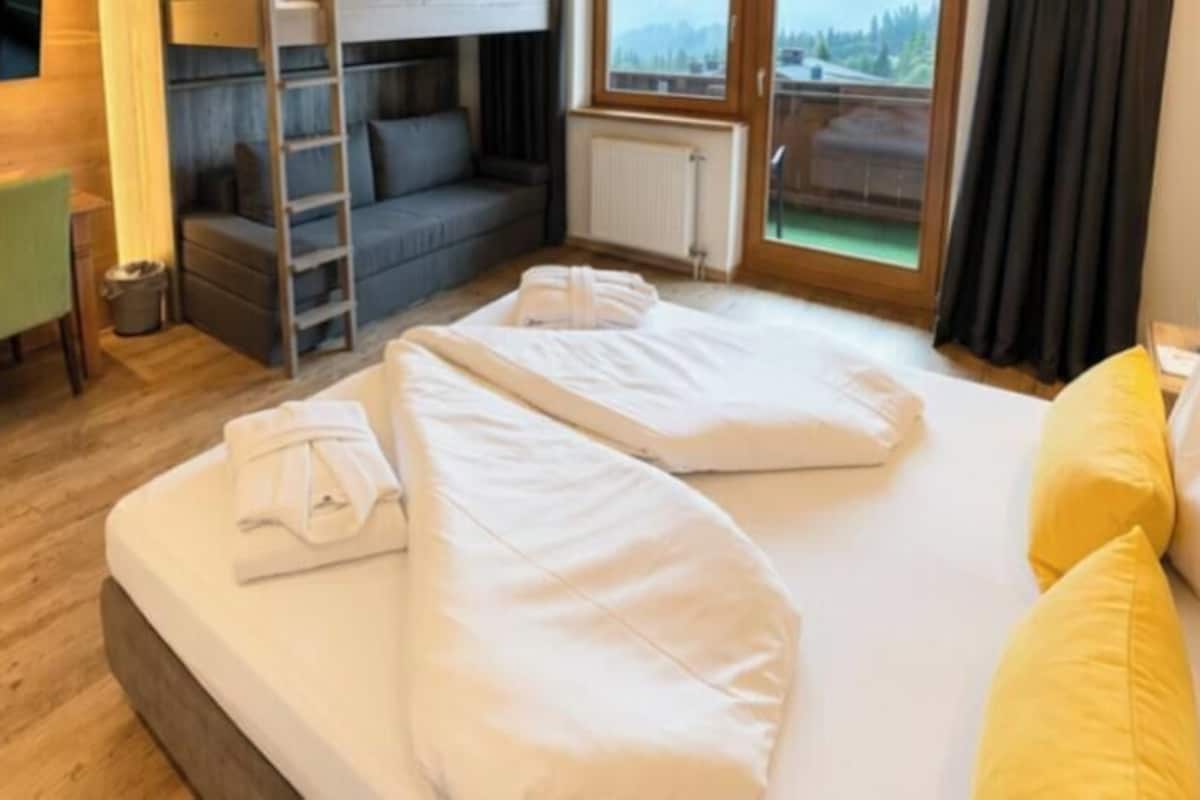 A hotel room with a bed, a desk with chairs, a TV, and a view of the outdoors.