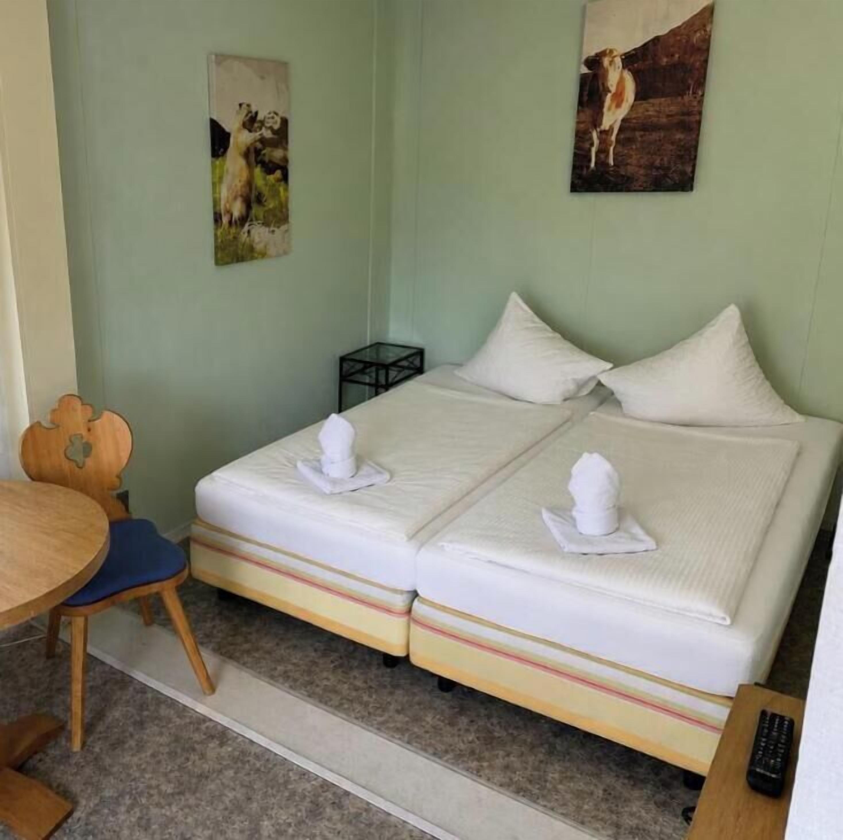 Una habitación con una cama, una silla, una mesita y dos cuadros en la pared.