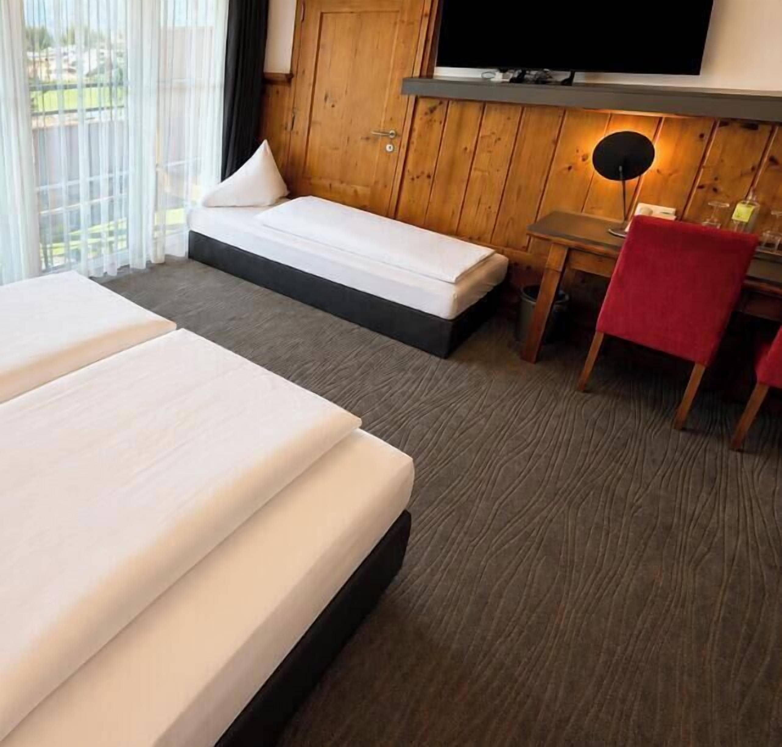 A hotel room with two beds, a desk, a chair, and a television.