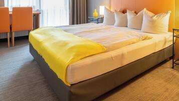 A hotel room with a bed, a desk, two chairs, and a nightstand with a lamp.