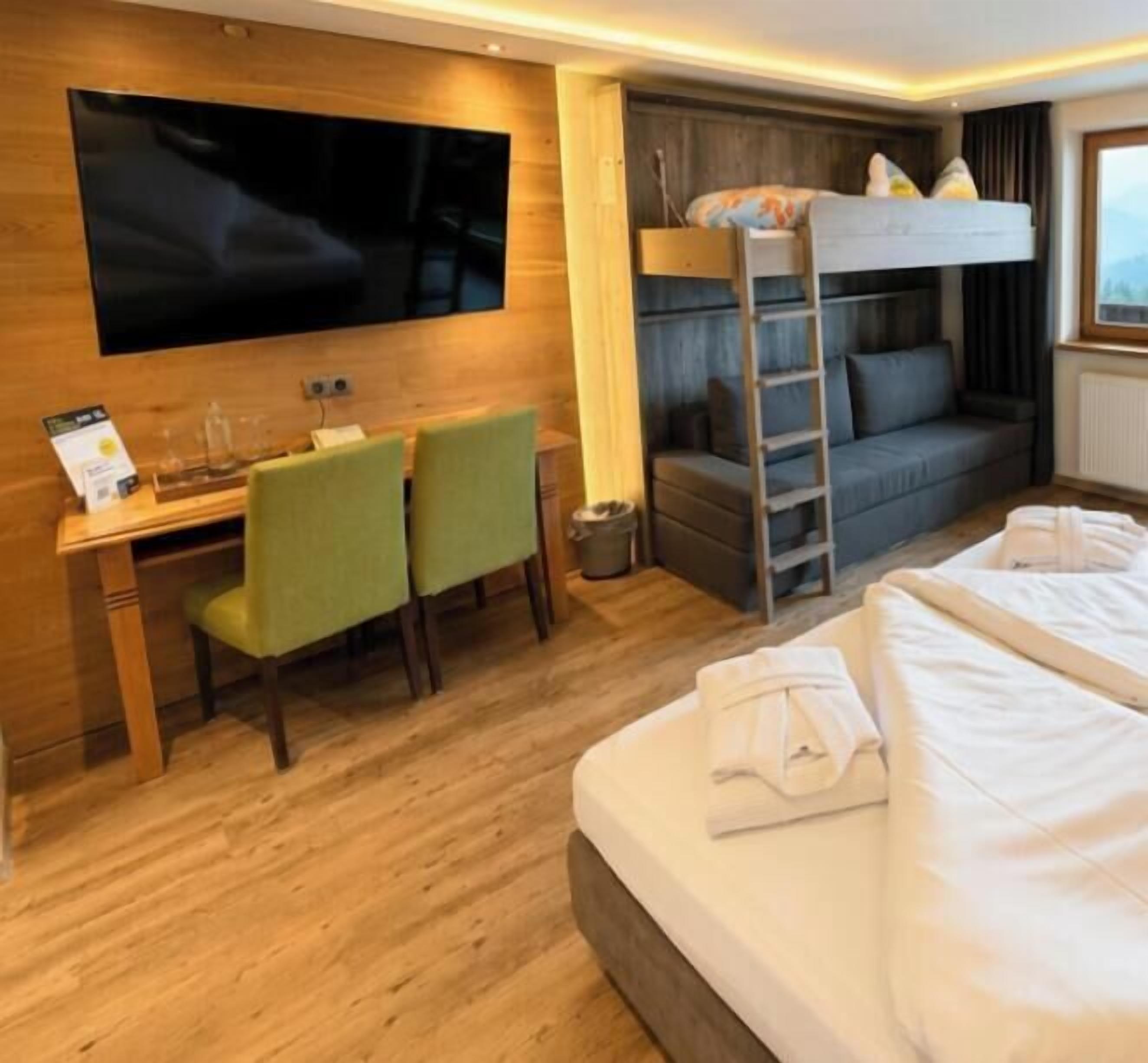 Una habitación de hotel con literas, un escritorio con dos sillas, un televisor y una cama con toallas.