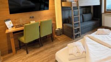 Una habitación de hotel con literas, un escritorio con dos sillas, un televisor y una cama con toallas.