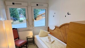 Une petite pièce avec un lit, une chaise, une table et une fenêtre.