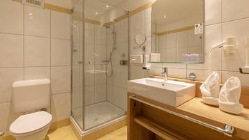 Un baño moderno con ducha envuelta en vidrio, inodoro blanco, lavabo con espejo y tocador de madera.