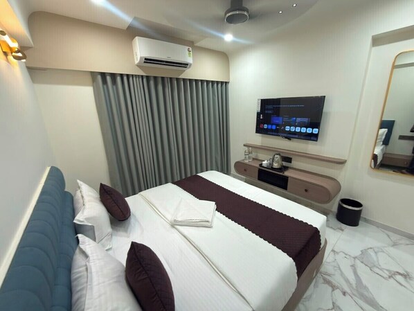 A modern hotel room with a large bed, a flat-screen TV, a desk with a chair, and a mirror.