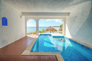 Ein Schwimmbecken mit Blick auf den Ozean, einen Strand und einen Reetdachschirm.