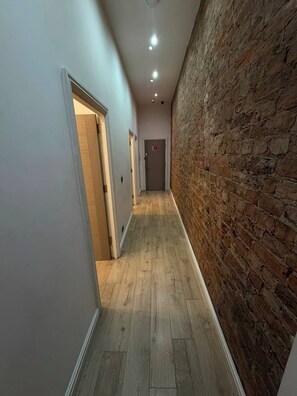 A hallway with a wooden floor, a brick wall on one side, and doors leading to rooms. - Sweeting Street Apartments (Liverpool)
