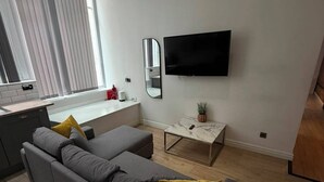 Ein modernes Wohnzimmer mit grauem Sofa, einem flachbildfernseher an der Wand und einem kleinen Tisch mit einer Pflanze.