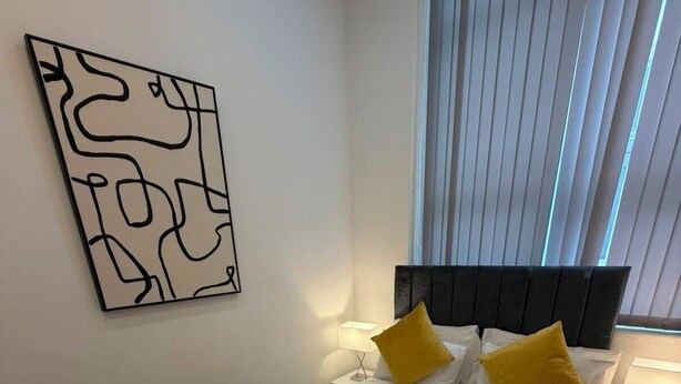Ein Hotelzimmer mit einem Bett, einem Nachttisch, einer Lampe und einem Fenster mit Jalousien.