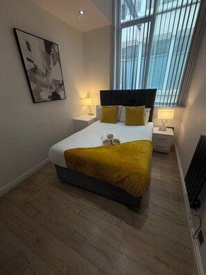 A modern bedroom with a bed, two bedside tables, a window, and a wall-mounted picture. - Sweeting Street Apartments (Liverpool)